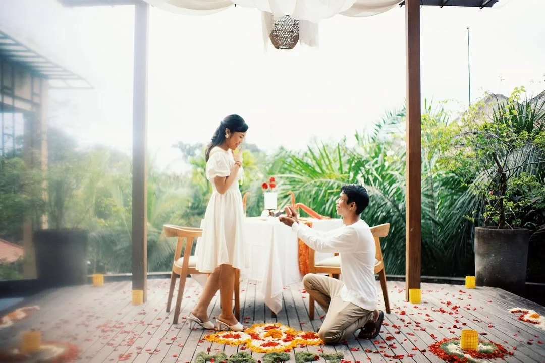 Bride standing beside her kneeling groom in a bright ceremony room