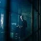 A moody urban night scene featuring a silhouetted figure in a dimly lit alleyway with vibrant city lights in the background.