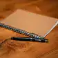 Elegant leather-bound notebook with pen on wooden desk, perfect for note-taking and journaling.