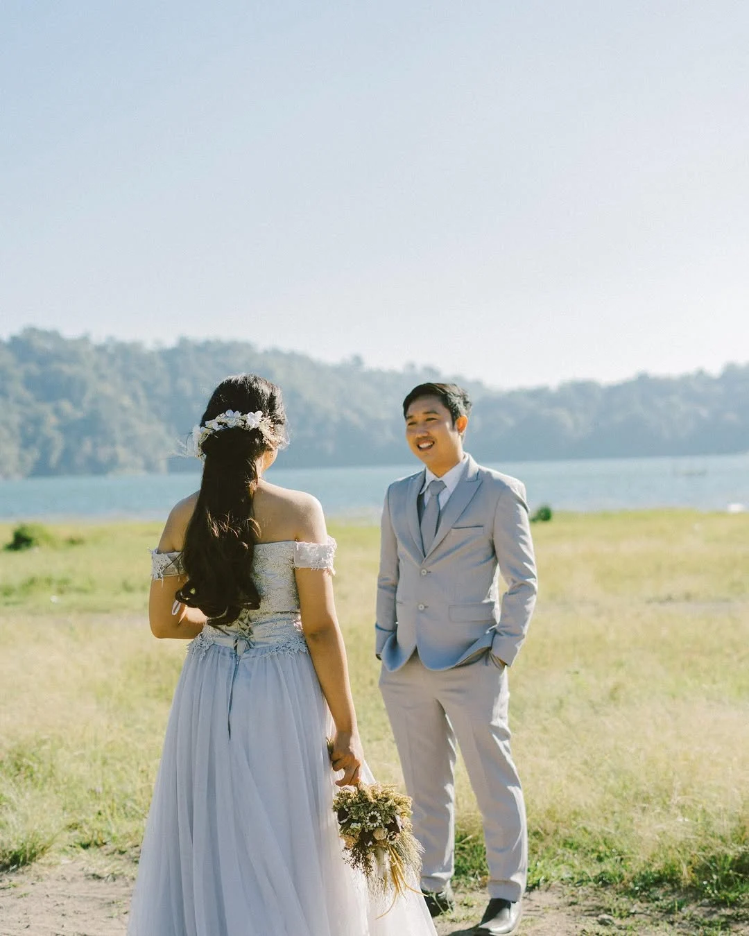 Bride and groom facing one another in a sunlit field in Bali
