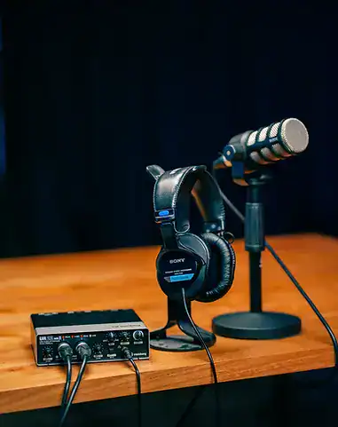 High-quality podcast recording equipment on a wooden table with microphone, headphones, and audio interface.