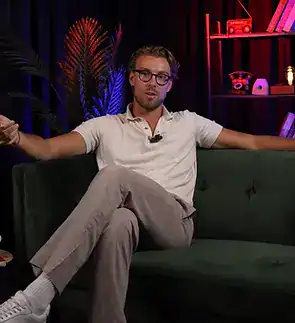 Modern man in white casual outfit seated on dark green sofa at Villo Studio interview.