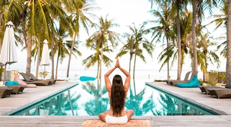 Femme sereine en méditation au bord d'une piscine à débordement tropicale, idéale pour les retraites bien-être et le tourisme expérientiel à Bali.