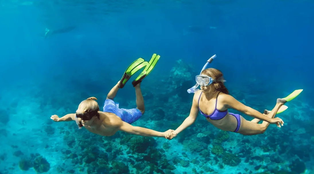 Bright underwater couple snorkeling with fins and masks in vibrant coral reef scene.
