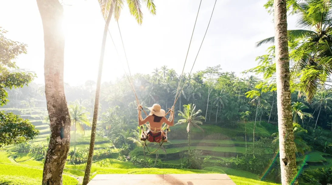 Serene woman on swing overlooking lush tropical rice terraces in Bali, Indonesia.