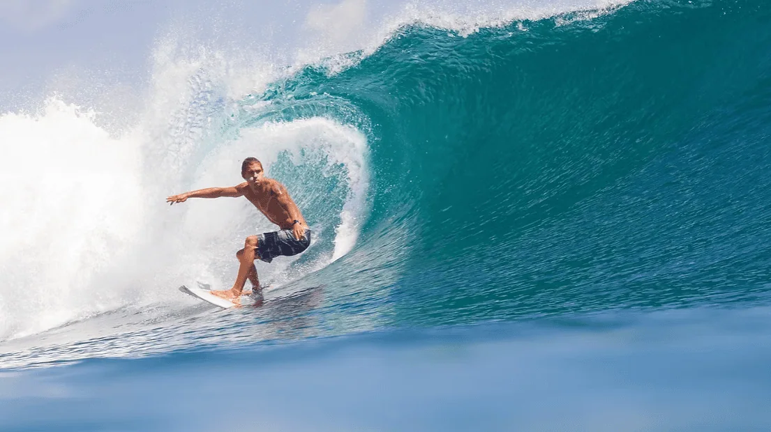 Surfer riding a wave at sunset on a famous Bali beach.